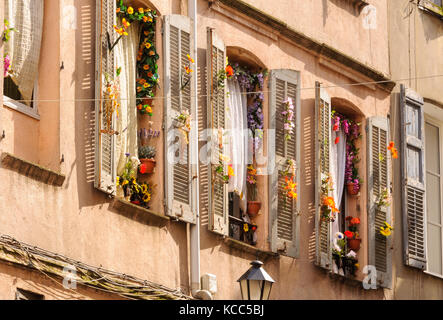 Windows and shutters decorated with colorful fake flowers - Grasse, France Stock Photo