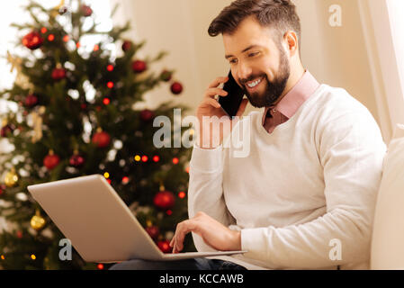 Pleasant man making phone call while using laptop Stock Photo