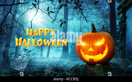 Happy Halloween lettering on creepy old cemetery with cool blue moonlight and a glowing Jack o lantern Stock Photo