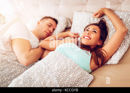 Beautiful loving couple in bed in the morning. Girl stretching next to her sleeping boy. Stock Photo
