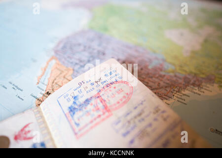 (Selective focus) A passport with stamps is on a blurred geographical map of the world. The passport shows some entry stamps in various countries arou Stock Photo