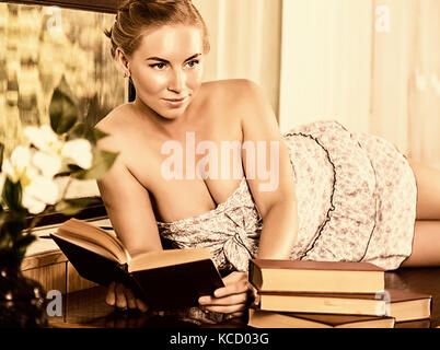 young woman reads a book lying on a desk in front of a window. old style, lolita concept Stock Photo