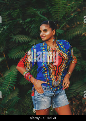 Afro-american woman outdoor. Multi ethnic girl wearing colorful clothing posing, enjoys the nature. Green tropical background Stock Photo