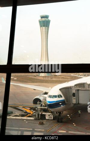 Kunming Changshui International Airport, Yunnan, China. Control tower and passenger airplane on apron preparing for flight seen from concourse window Stock Photo