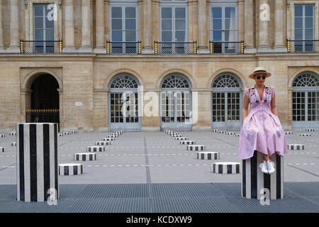 PARIS, France, June 16, 2017 : A tourist woman sits in the larger inner courtyard of Palais-Royal, the Cour d'Honneur, and its art piece known as 'Les