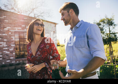 Multi-ethnic millennial couple walking outdoors and chatting. Man and woman with a drink at outdoors party. Stock Photo
