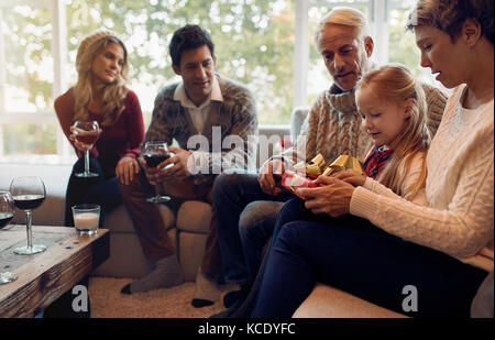 Little girl sitting in living room with family opening christmas presents. Extended family gathering on christmas eve. Stock Photo
