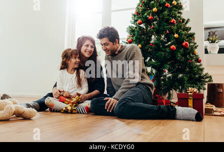 Family sitting beside Christmas tree opening gifts. Small family having happy time together on Christmas. Stock Photo