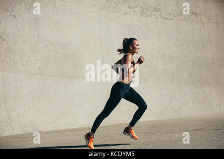 Healthy young woman running in morning. fitness model exercising in morning outdoors. Full length side view shot. Stock Photo