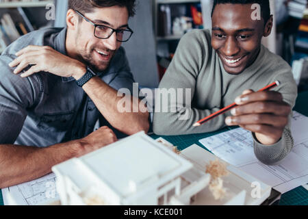 Two coworkers discussing housing model in office. Architects working on a building model. Stock Photo