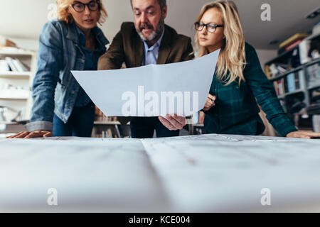 Group of architects discussing over blueprints in office. businessman working with female colleagues and pointing at construction plan. Stock Photo