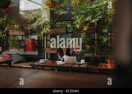 Two women sitting with a laptop and notepads at a table. business colleagues working while having coffee. Stock Photo