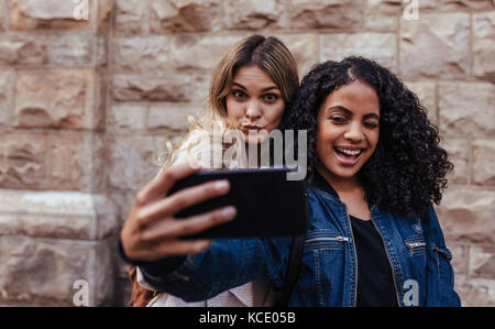 Happy girls taking a selfie using mobile phone. Women making faces while posing for a selfie. Stock Photo