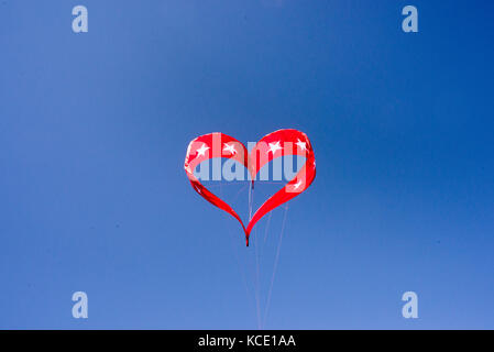 A red heart shaped kite flies in the blue sky Stock Photo