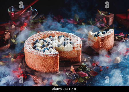 Cut cake with a shortbread crust on a dark background. A piece of cake with whipped cream and blueberries. Traditional pumpkin pie in a Halloween still life with pastry. Stock Photo