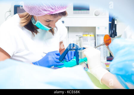 A female dentist in white medical uniform and her assistant make a procedure for the treatment of teeth from dental caries and clears teeth from a den Stock Photo