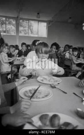 1970s, historical, picture shows a young boy sitting eating his school dinner at a table with other chldren at Langbourne Primary School. Dulwich, London, England, UK. Stock Photo