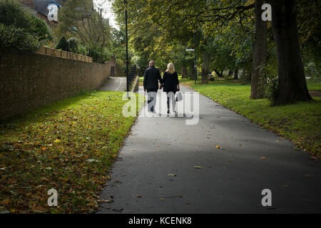 Mature couple, holding hands, stroll together along quiet, scenic, tree-lined, riverside footpath in early autumn - New Walk path, York, England, UK. Stock Photo