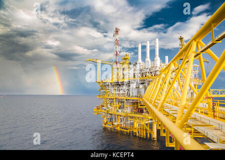 Dark cloud, blue sky and rain with rainbow near oil and gas central processing platform in the morning. Stock Photo