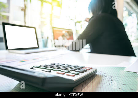businesswoman using laptop and calculator at office desk and many document data graph in morning light, business concept. Stock Photo