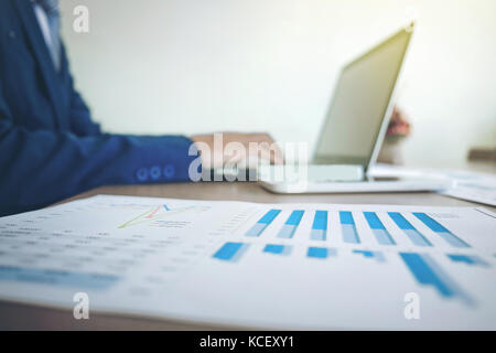Image of business, Business man working at office with laptop and graph data documents on his desk, blurred background. Stock Photo