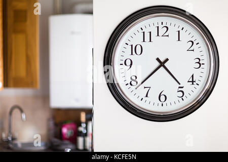 Large clock face on white kitchen wall with out of focus kitchen background Stock Photo