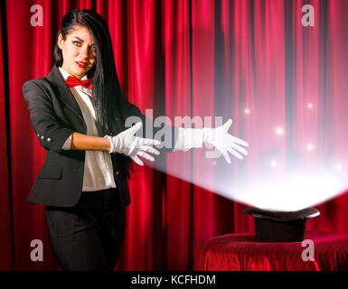 Beautiful young magician showing to a hat with lights and fumes going out Stock Photo