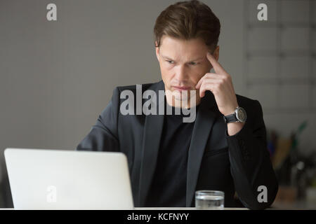 Perplexed or puzzled handsome businessman looking at laptop screen. Thoughtful project manager double checking important financial information, result Stock Photo