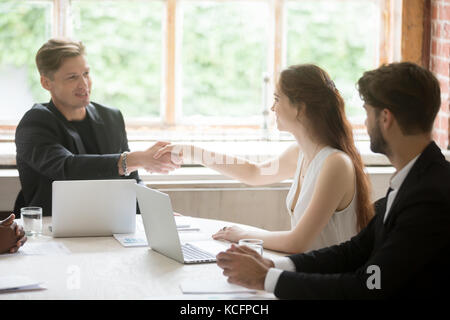 Young male executive in formal suit shaking hands with attractive female coworker. Employees greeting each other before corporate meeting, briefing ab Stock Photo