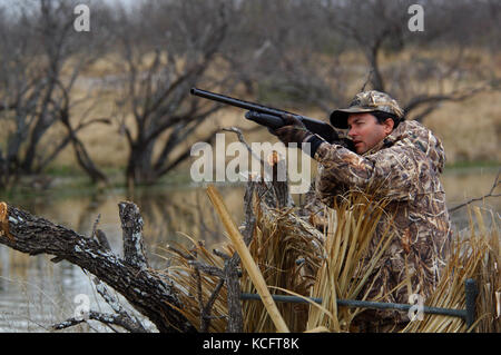 A duck hunter aiming and shooting at ducks from a blind in South