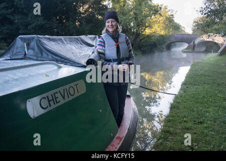 Crew member on a hired narrowboat as an early morning autumn mist begins rising on the Oxford Canal by Bridge 45 near Newbold on Avon.