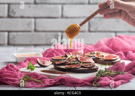Fresh bread with figs, ricotta and honey on white cutting board Stock Photo