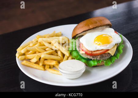 Meat Burger with egg, sauce and fries on the blsck table Stock Photo