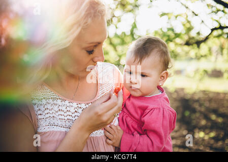 Mother with baby Picking and eating Cherry In Garden Stock Photo
