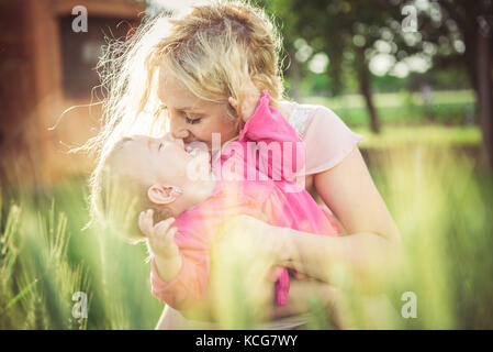 Young mother holding and kissing her baby in the grass Stock Photo