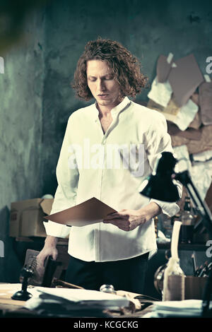 Writer at work. Handsome young writer standing near the table and making up something in his mind Stock Photo