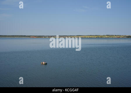 Young man and woman in natural sunlight float on a lake in a rubber dinghy sailing boat Stock Photo