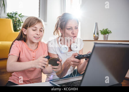 Mother and daughter playing video games on laptop at home Stock Photo