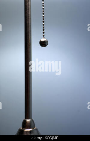 Ball and chain light switch in metal chrome hangs next to a lighting column against a blue background Stock Photo