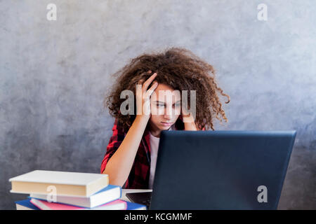 Indisposed teenage girl sitting in front of laptop computer at home Stock Photo