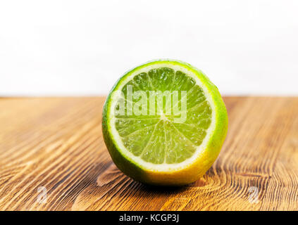 a cut piece of sour green lime lying on a brown wooden table. Photo close-up. Focus on fruit Stock Photo