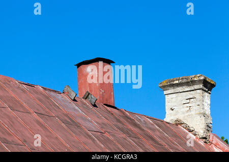 The old roof is covered with metal sheets with old two chimneys. one chimney with rusting metal sheets. The second is made of bricks and is destroyed Stock Photo