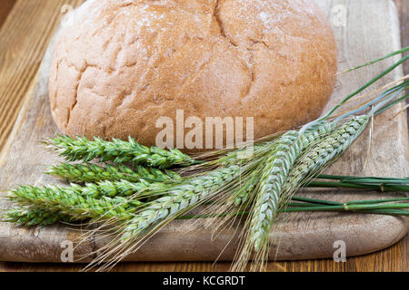 green ears of wheat and rye lying together with a freshly baked loaf of home-made bread. photo close up Stock Photo