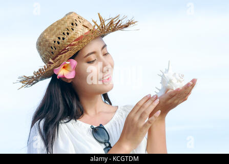 Asian woman listening sea with seashell at beach. Stock Photo