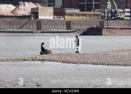 Woman sitting on flotsam tree trunk, River Rhine, near Cologne Germany ...