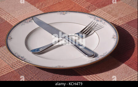 A fall place setting with a knife and fork crossed on the plate on a plaid table cloth Stock Photo