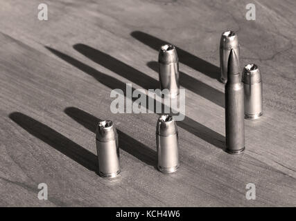Five 40 caliber hollow point bullets with one 223 FMJ round on a wooden table in black and white Stock Photo