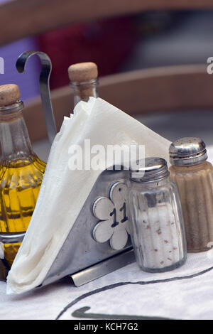 typically greek condiments on a table with napkins on a table place setting at a tavern with olive oil and dressings for food when eating in Greece. Stock Photo