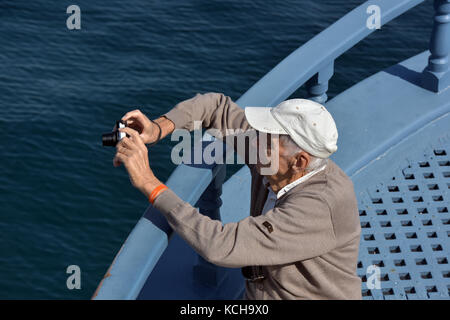 An elderly man on holiday taking a photograph on a boat trip. Stock Photo