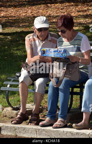 two middle aged or older people or a couple reading a tourists map sitting on a bench in the greek town of Kerkira. sharing a map together Stock Photo
